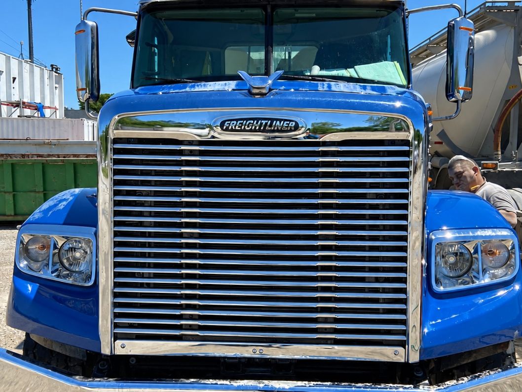 Blue Freightliner from the front with a bright chrome grille and bumper.