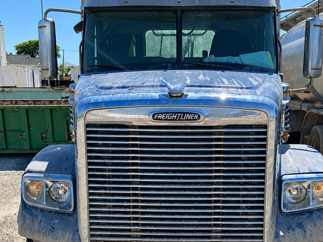 Blue Freightliner from the front with a dusty grille and a dull bumper.