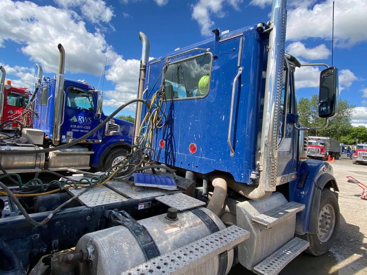 Blue tractor cab with road film and dust on the cab, the fuel tank and the step plates.