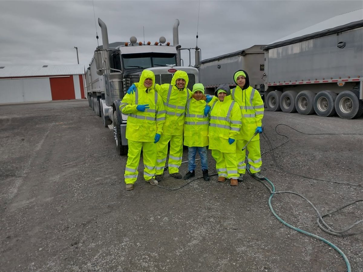 Five smiling crew members in bright rain suits and blue gloves posing together in front of a truck.
