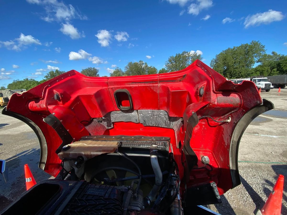 Engine bay of a red tractor with the hood tipped forward, showing the clean underside and radiator.