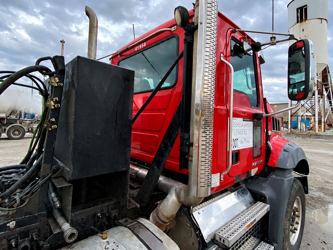 Red Mack cab beside a chrome stack with bright steps and an aluminum fuel tank below it.