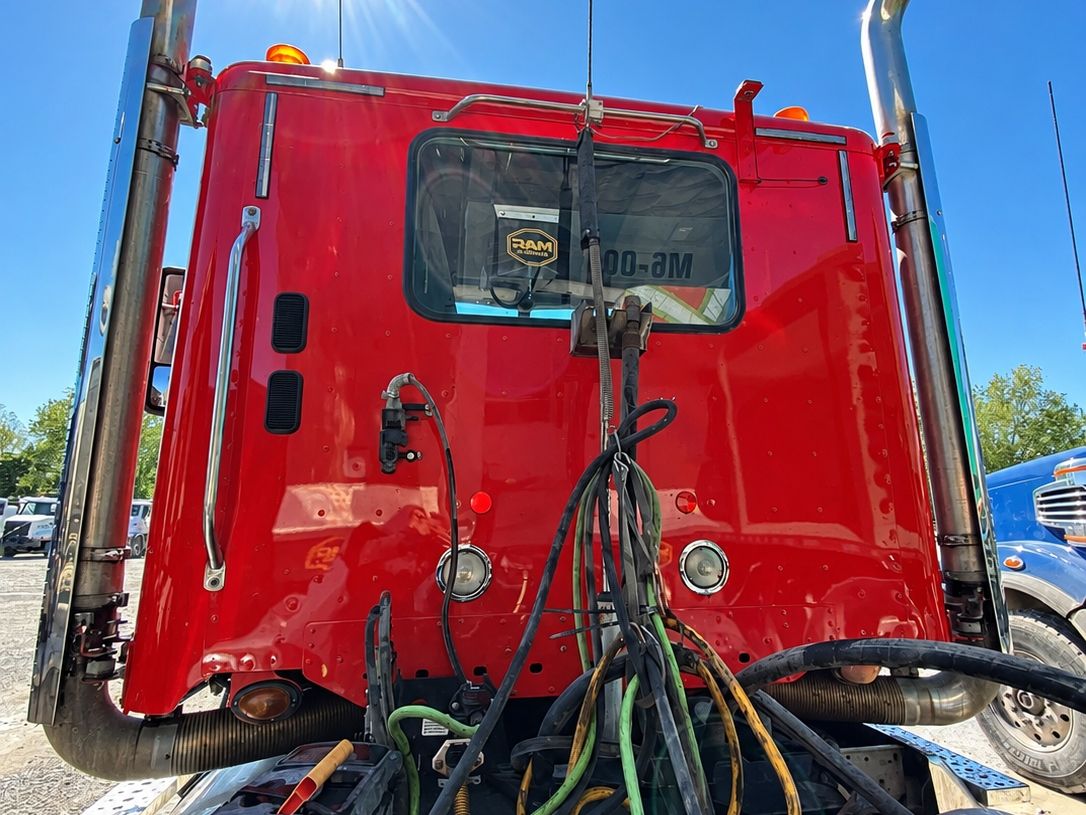 Back of a clean red tractor cab with chrome stacks and hoses over the deck, the sun flaring above it.