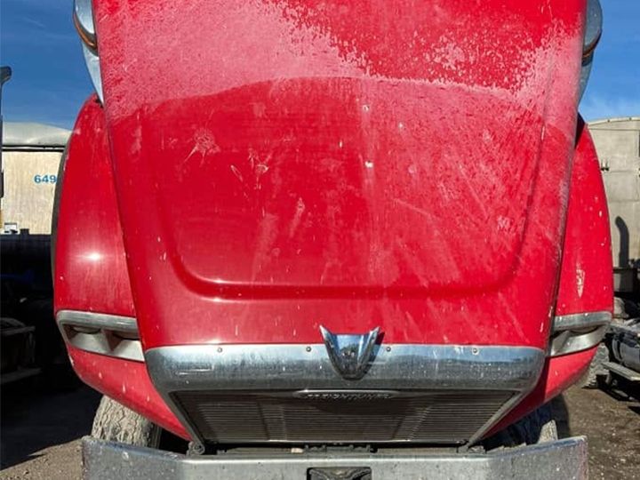 Red truck with the hood raised and the hood and bumper dull under dried white spray and spots.