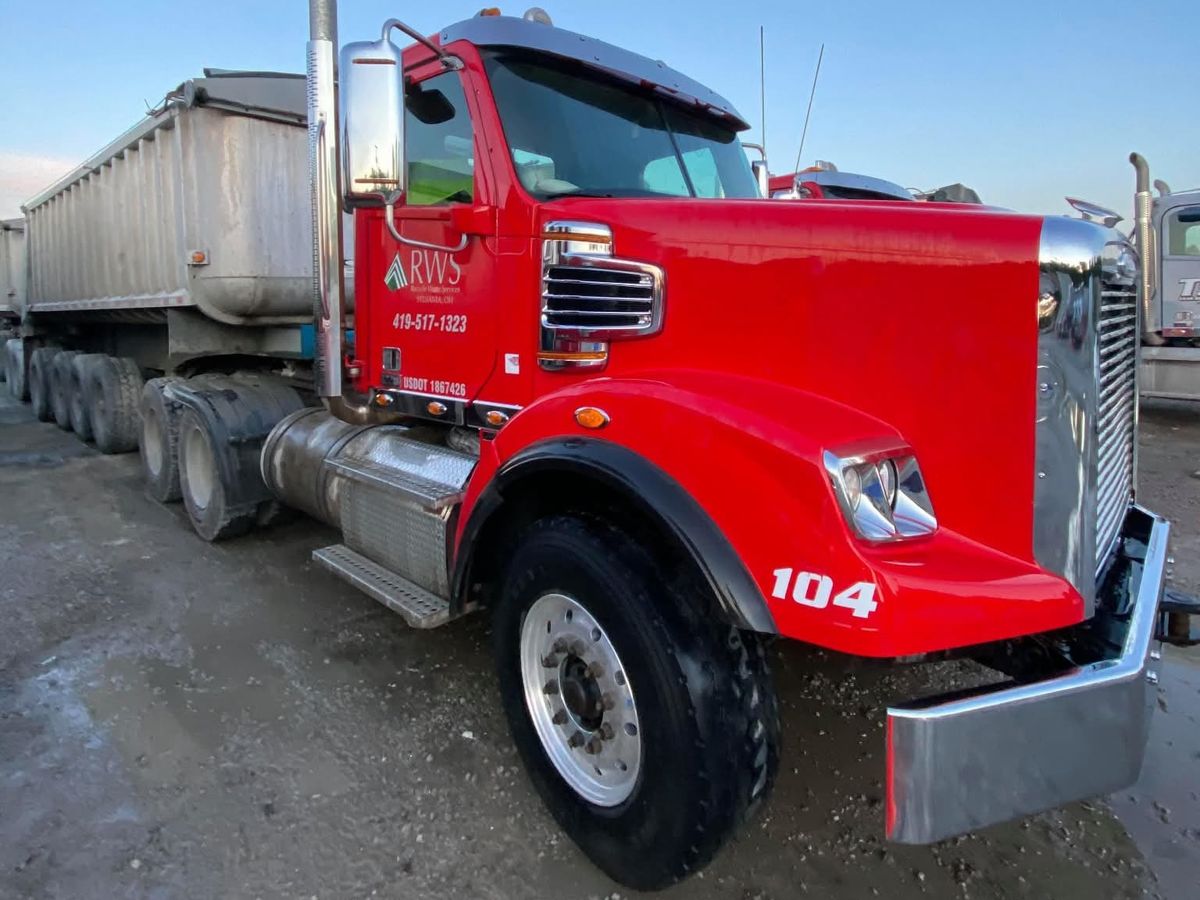 Red tractor numbered 104 with a company logo on the cab door and a long dump trailer behind it.