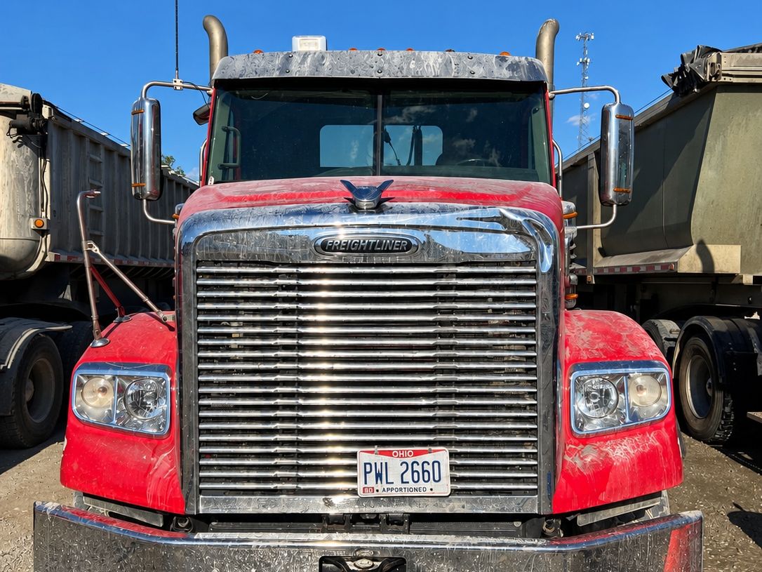 Red Freightliner from the front with a dusty grille and a dull bumper.