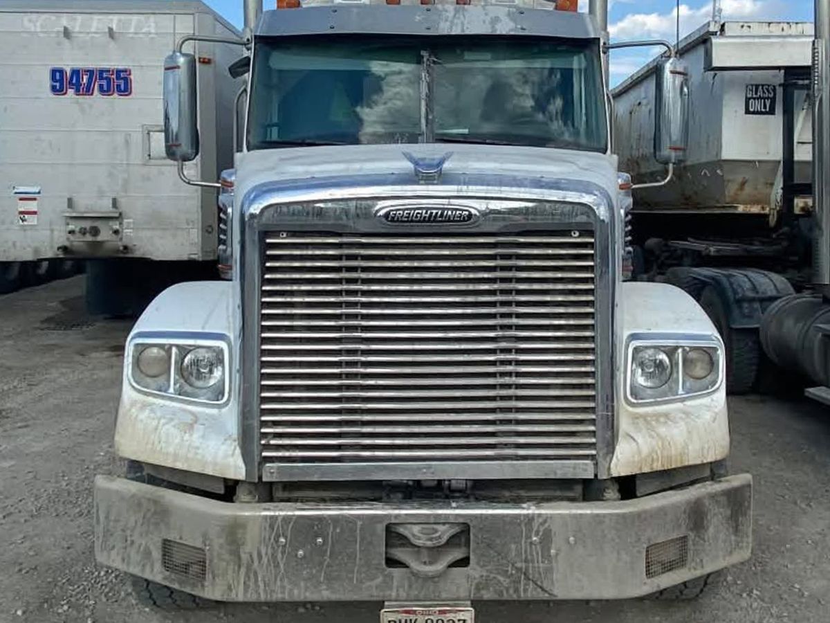 White Freightliner from the front with mud streaks on the fenders and a dull bumper.