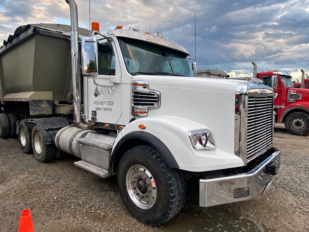 Clean white Freightliner with bright chrome and a dump trailer behind it at dusk.
