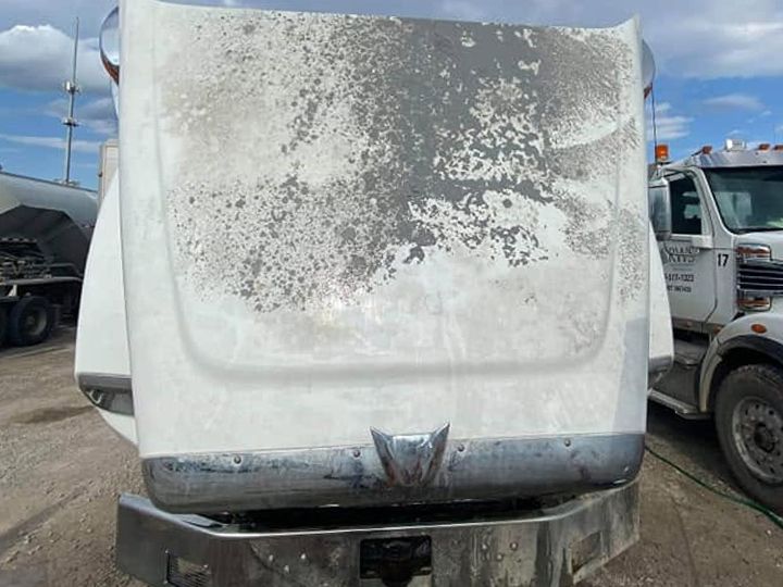 White truck with its hood raised and gray road film and spotting across the hood.