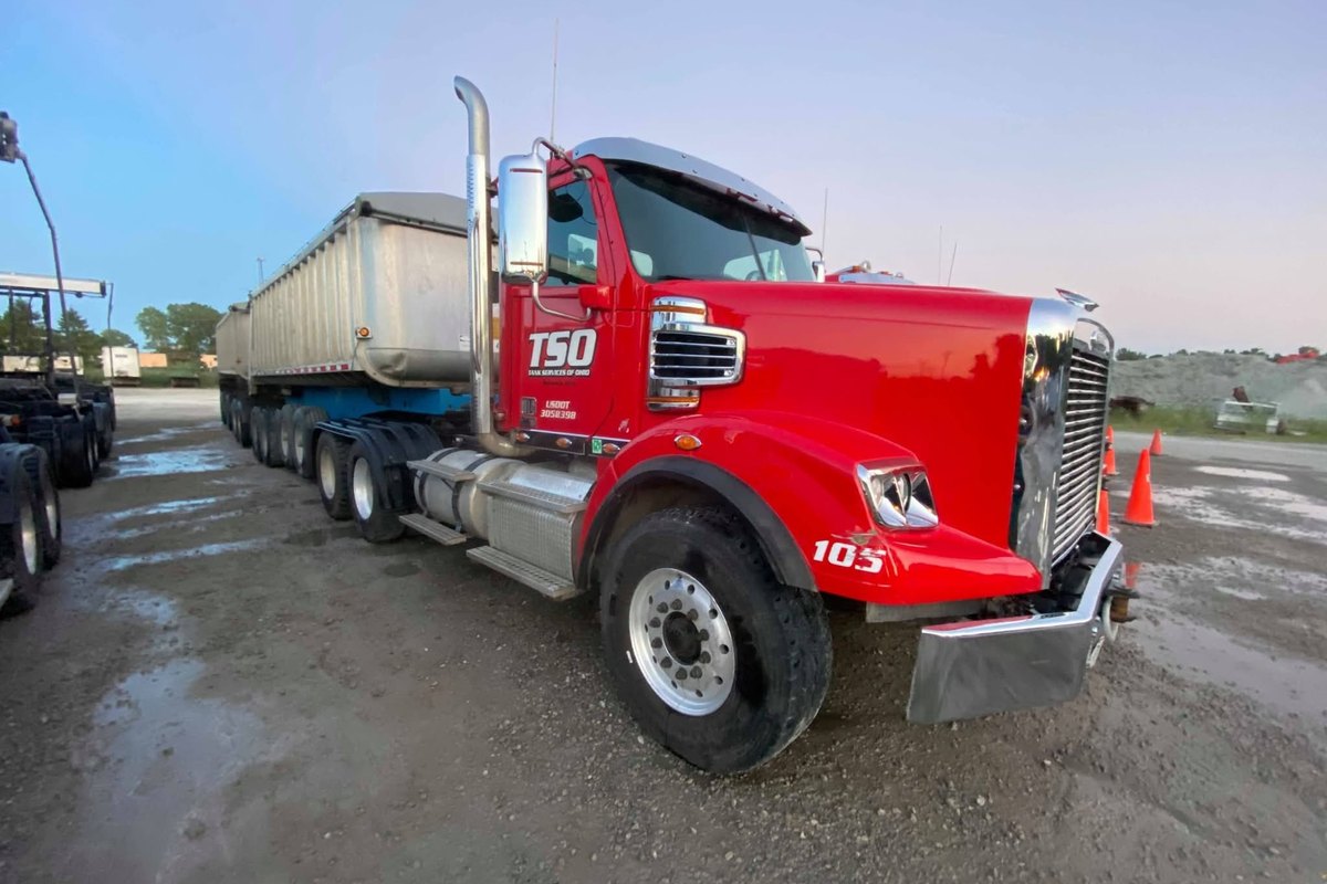 Clean red Freightliner dump-truck tractor numbered 105 with a polished wheel and an aluminum dump trailer behind it.