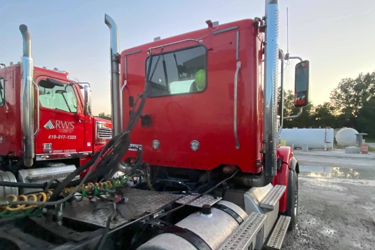 Rear-quarter view of a clean red Freightliner cab with tall polished stacks and a shining aluminum fuel tank.
