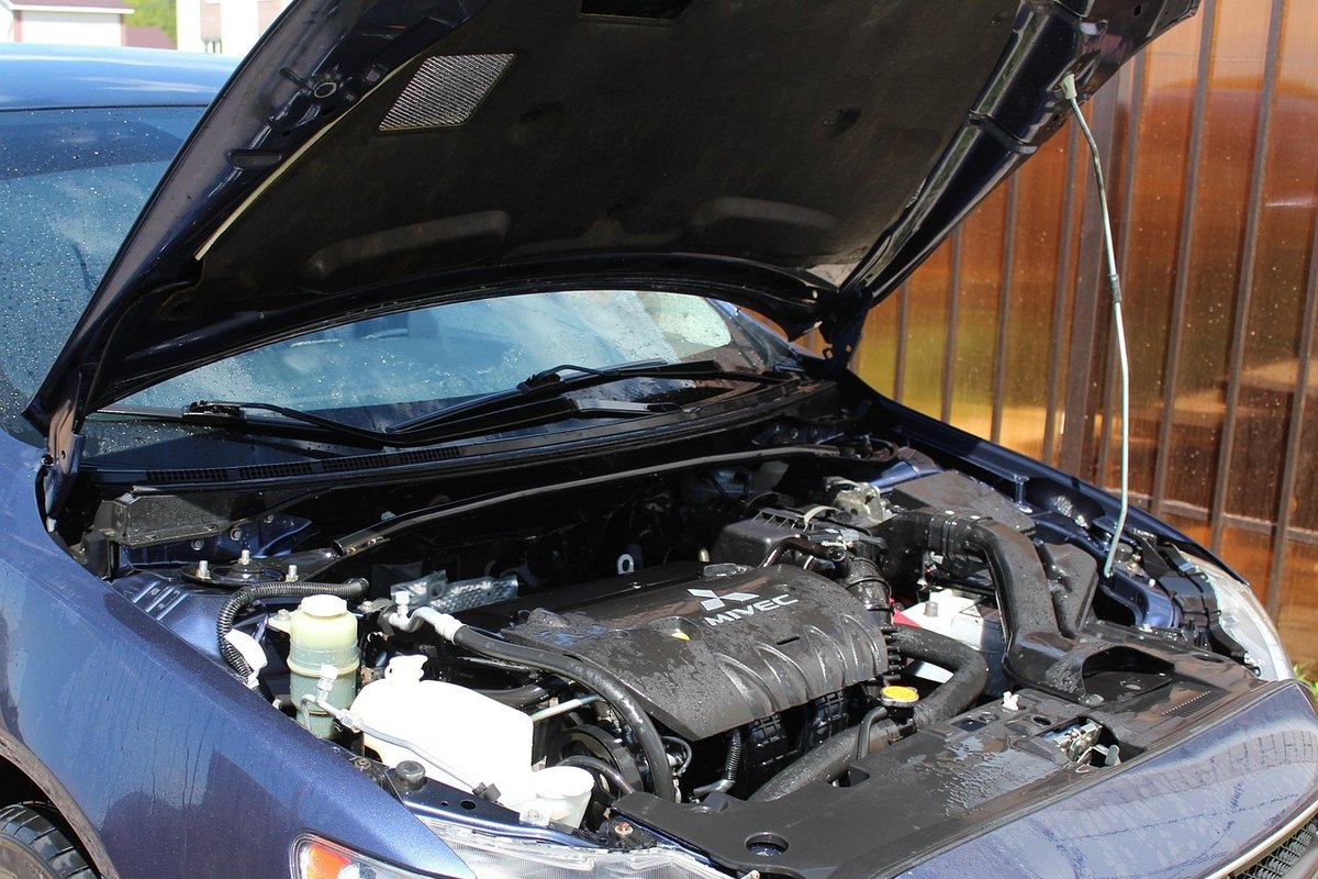 Wet, freshly rinsed engine bay under the raised hood of a dark blue car, with water drops on the engine cover.