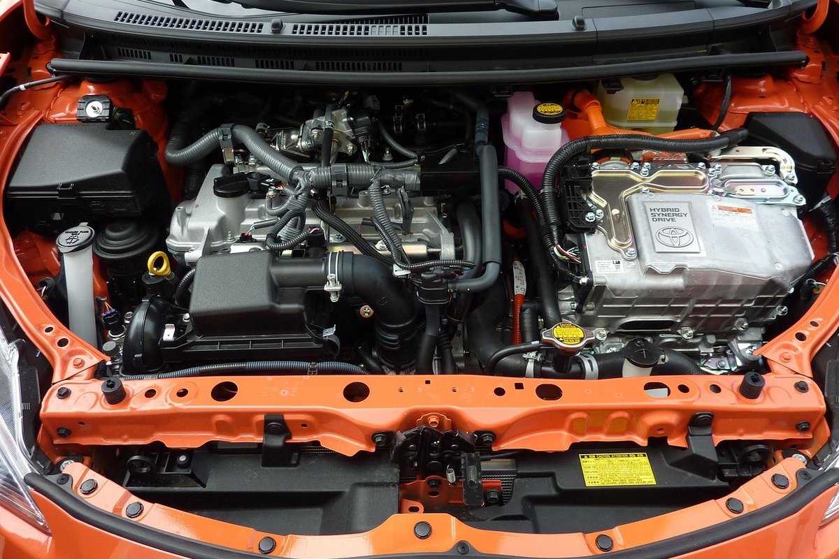 Clean engine bay of an orange hatchback with black hoses, a silver inverter unit and fluid reservoirs with yellow caps.