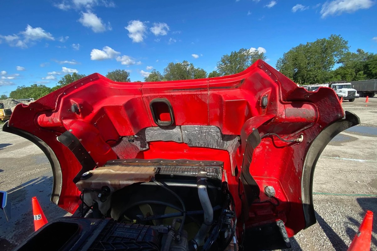 View into the engine bay of a red truck with the hood tipped forward, showing the radiator, hoses and the top of the engine.