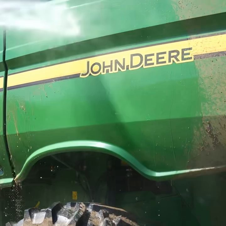 Glossy green combine body panel with a yellow stripe, freshly rinsed by pressure washer spray with water running down.