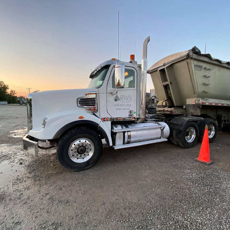 Clean white tractor with polished wheels and a chrome stack beside a dump trailer at sunset.