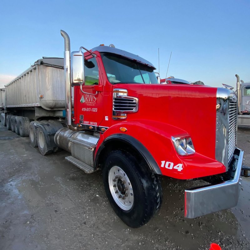 Red tractor numbered 104 with a company logo on the door and a long dump trailer behind it.