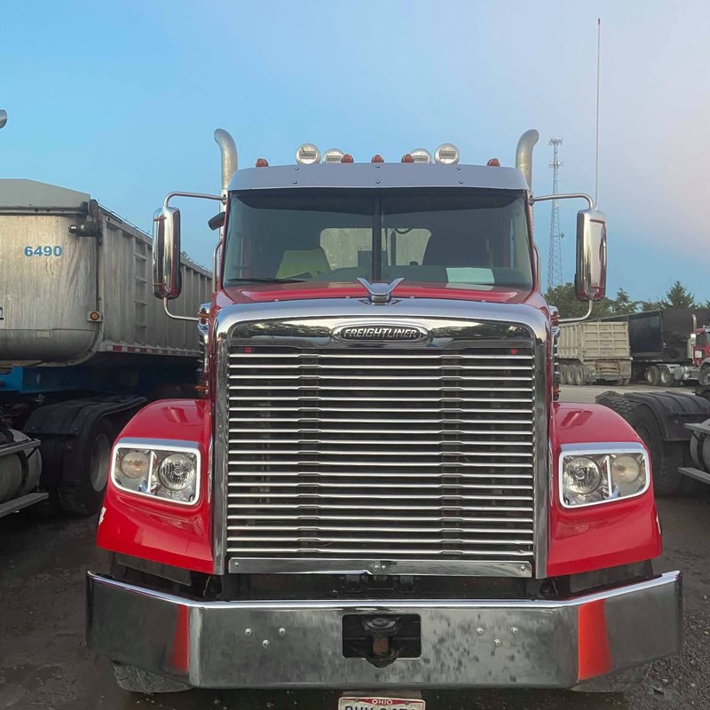 Red tractor facing the camera with a bright chrome grille and bumper beside a gray dump trailer.